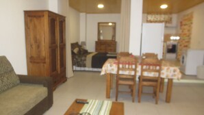 A living room with a sofa, wooden cabinet, dining table with chairs, and a kitchen area in the background. - Villa Lucinda ..... (São João)