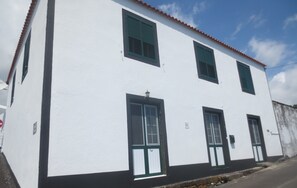 A white building with black trim and green shutters, featuring a stone foundation and a clear sky.