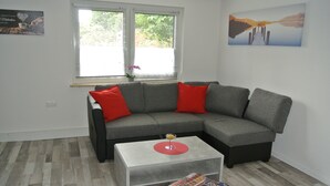 A modern living room with a grey sectional sofa, red cushions, a white coffee table, and a bookshelf. - Holidays, holidays and sea (Wilhelmshaven)