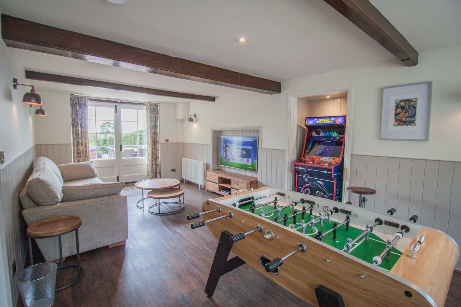 A cozy living room with a foosball table, a sofa, a TV, and a retro arcade game.