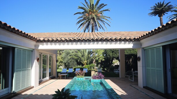 A pool area with tiled flooring, a palm tree, and a pergola structure. - Unique: magnificent villa in Porquerolles (Ile de Porquerolles)