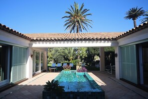 A pool area with tiled flooring, a palm tree, and a pergola structure. - Unique: magnificent villa in Porquerolles (Ile de Porquerolles)