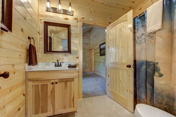 A wooden cabin bathroom with a sink, mirror, and toilet. - Splashin Bear Lodge, Pool in Cabin, Arcade Games, Pool Table, Hot Tub (Sevierville)