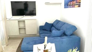 A modern living room with a blue sofa, a flat-screen TV, and a fruit bowl on the table. - VILLA GINEVRA COLICO (Colico Piano)
