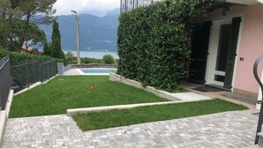 A paved patio with a small lawn area, a swimming pool, and a view of mountains. - VILLA GINEVRA COLICO (Colico Piano)