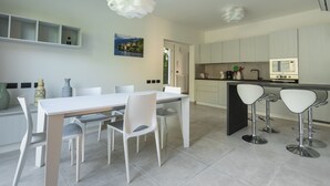 A modern kitchen with white cabinets, a central island with bar stools, and a dining area with a white table and chairs. - VILLA GINEVRA COLICO (Colico Piano)