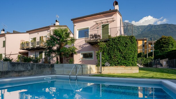 A swimming pool with a clear view of the surrounding buildings and a mountain in the background. - VILLA GINEVRA COLICO (Colico Piano)