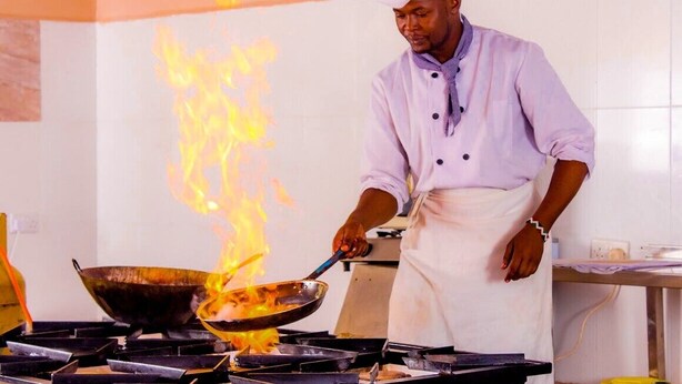 A chef cooking with a pan on a stove with flames.