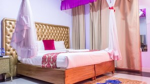 A bedroom with a tufted headboard, a bed with white bedding and a pink throw pillow, a wooden nightstand with a wicker basket, and a blue mat on the floor.