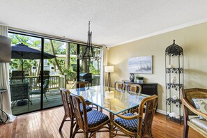A dining area with a glass table, wicker chairs, a black metal floor lamp, and a view of the outdoors.