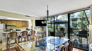 A dining area with a glass table and chairs, a kitchen with wooden cabinets, and a view of the outdoors. - Reduced Rates! Short Walk to the Beach and Pool! (Hilton Head Island)