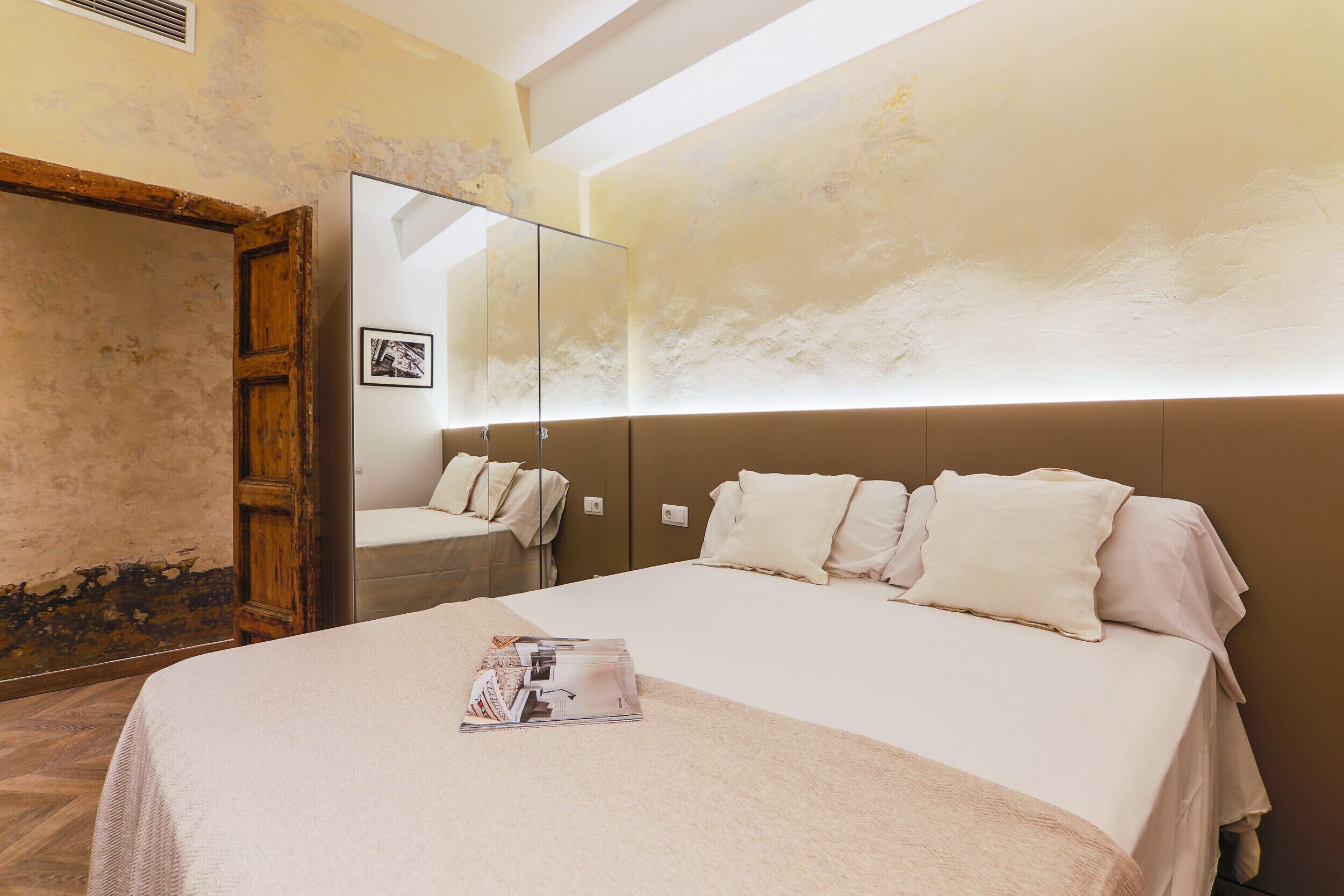 A hotel room with a large bed, a wooden wardrobe, and a mirror on the wall.