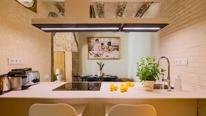 A modern kitchen with a central island, two bar stools, a sink, and a potted plant. - CASA CARME SEGUNDO (Barcelona)