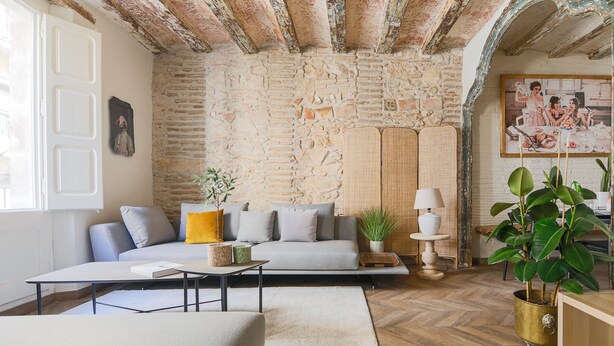 A cozy living room with a stone wall, a sofa, a coffee table, a lamp, and a potted plant. - CASA CARME SEGUNDO (Barcelona)