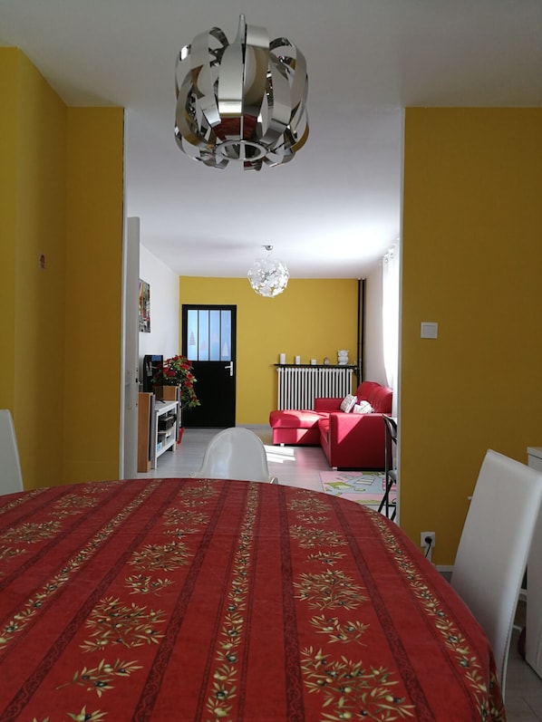 A room with a bed, a red sofa, a dining table, and a chandelier.
