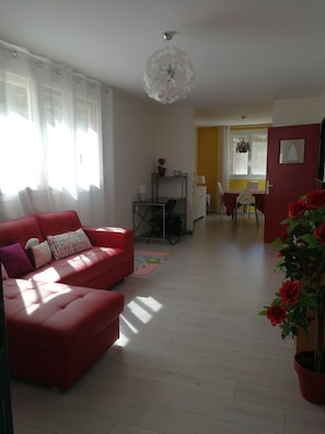 A living room with a red sofa, a dining area with a yellow wall, and a ceiling light fixture.