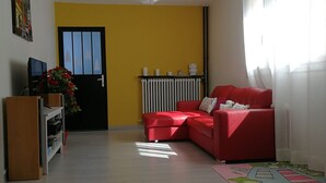 Ein Wohnzimmer mit rotem Sofa, einem Holzschrank, einer Heizung und einem Fenster mit durchsichtigen Vorhängen.