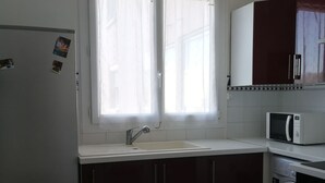 Eine Küche mit weißer Arbeitsplatte, dunklen Schränken, einer Spüle, einer Mikrowelle und einer Waschmaschine.