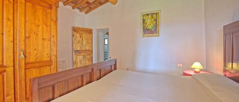 A bedroom with a wooden bed, a wooden wardrobe, a door, and a painting on the wall.