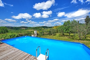 Ein Schwimmbecken mit Holzterrasse, umgeben von üppiger Vegetation und einer malerischen Aussicht auf sanfte Hügel.