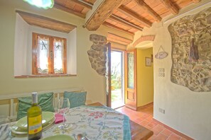 Una habitación con una cama, una mesa con una botella y un vaso, una ventana con cortinas y una pared de piedra.
