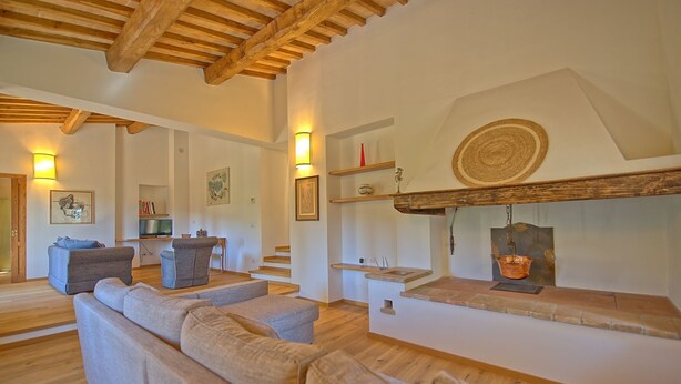 A spacious living area with a high ceiling, wooden beams, and a fireplace. There are sofas and a television in the room.