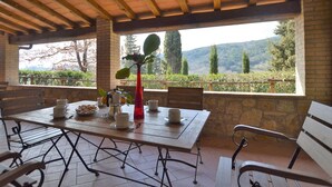 An outdoor patio with a table set for dining, stone walls, and a view of the countryside.
