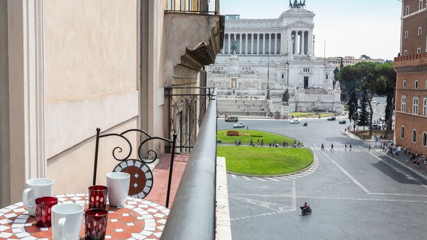 A balcony with a tiled table and four mugs, overlooking a city square with a large monument and a roundabout. - Amazing Piazza Venezia Suite Int 20 (Roma)