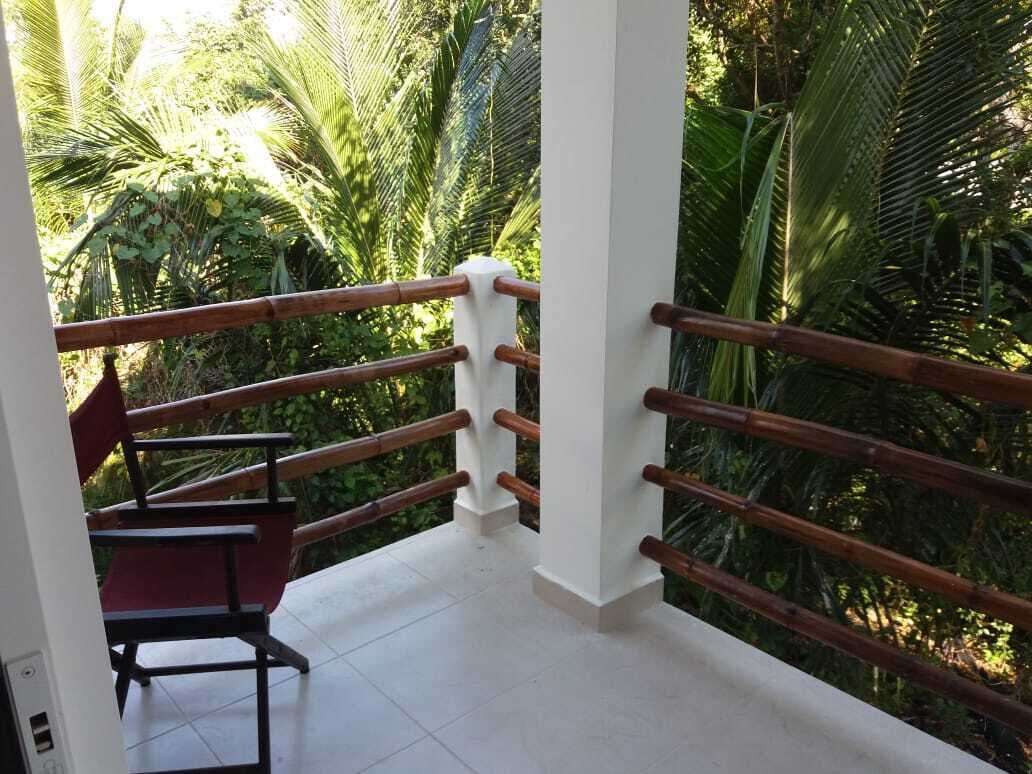 A balcony with a wooden railing, a red chair, and lush greenery in the background.