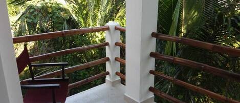 A balcony with a wooden railing, a red chair, and lush greenery in the background.