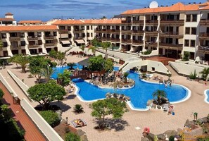 A hotel with a large swimming pool, multiple balconies, and a view of the ocean.