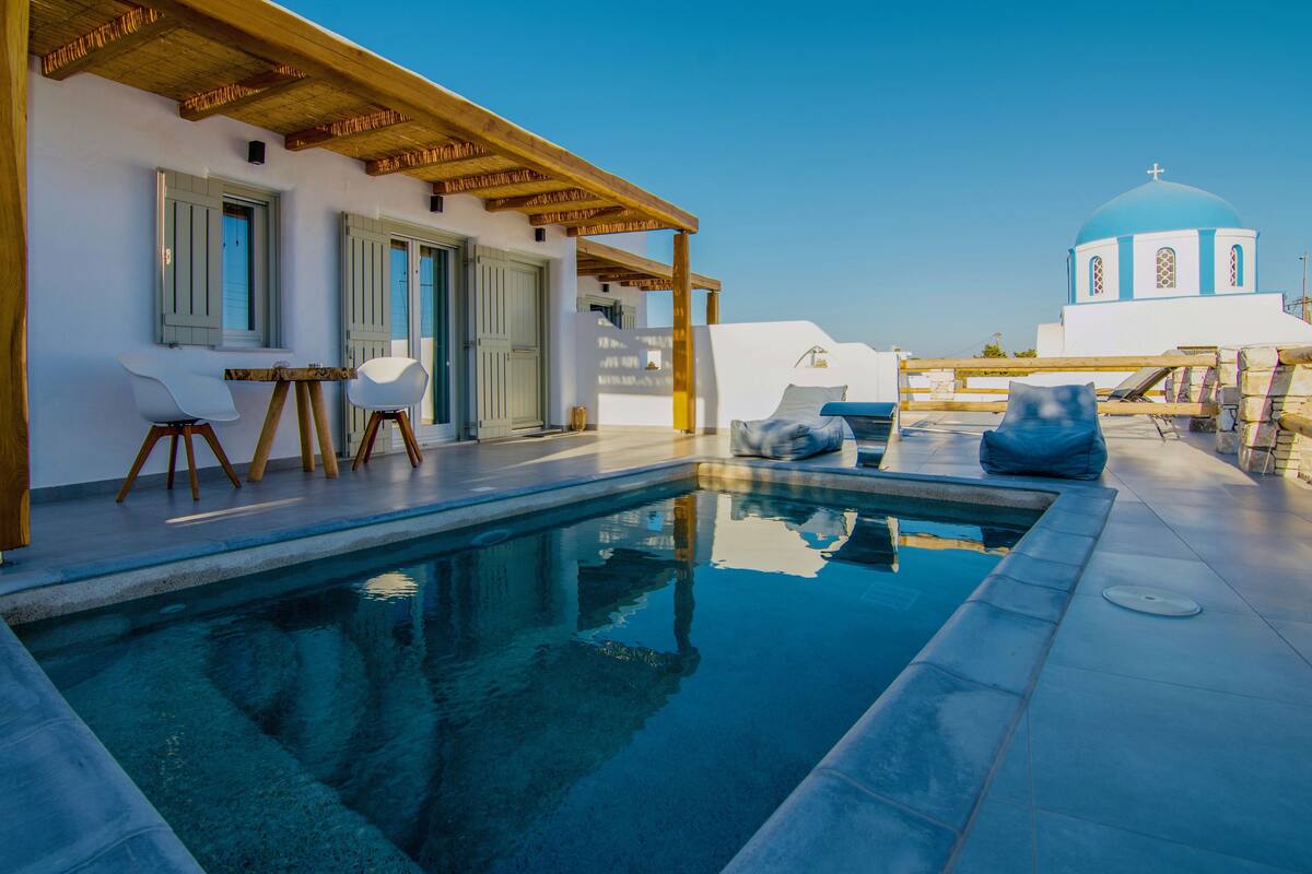 A pool area with a wooden pergola, white walls, and a blue-domed building in the background.