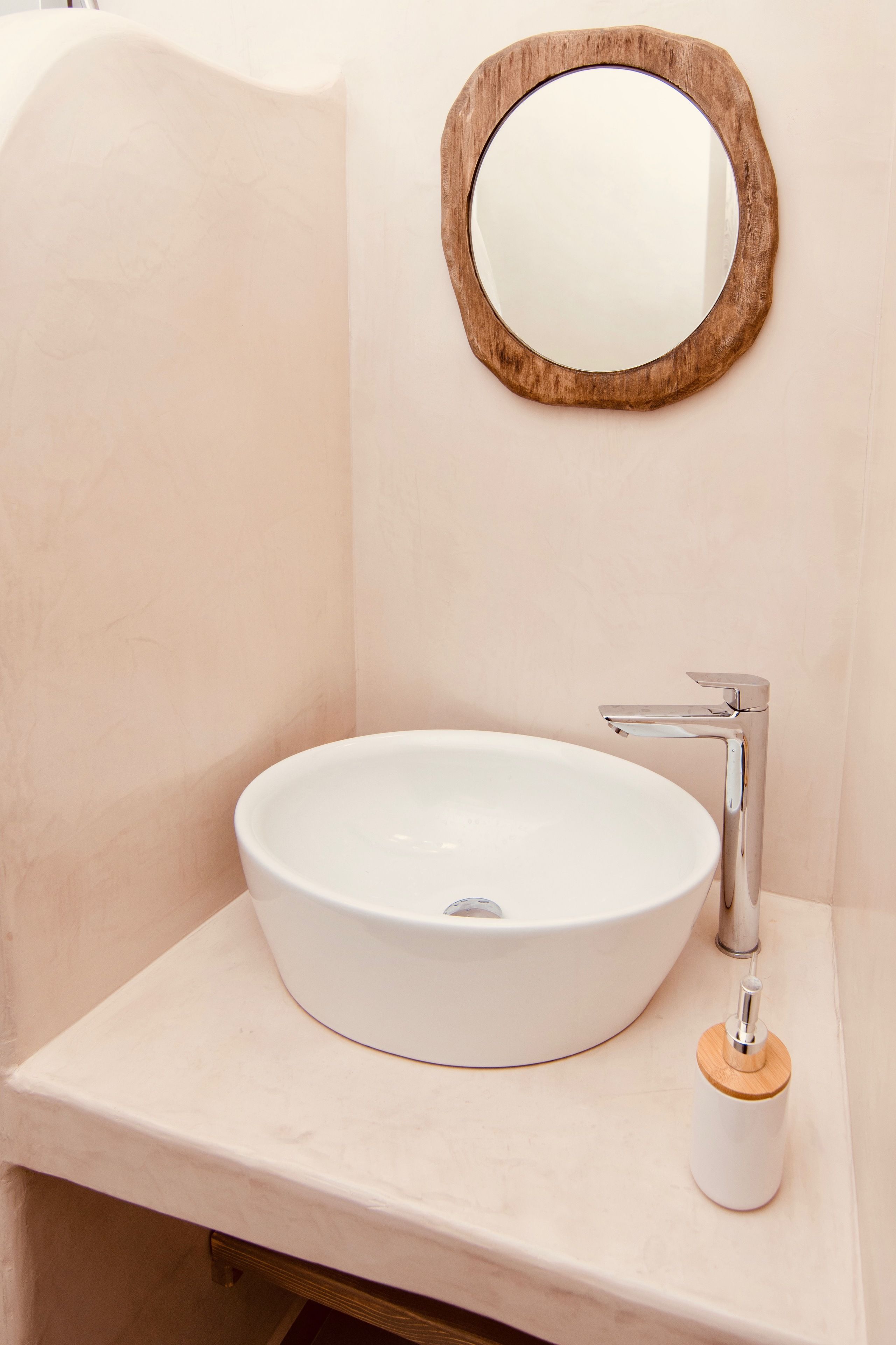 Un baño con un lavabo blanco redondo, un espejo con marco de madera y un grifo moderno.