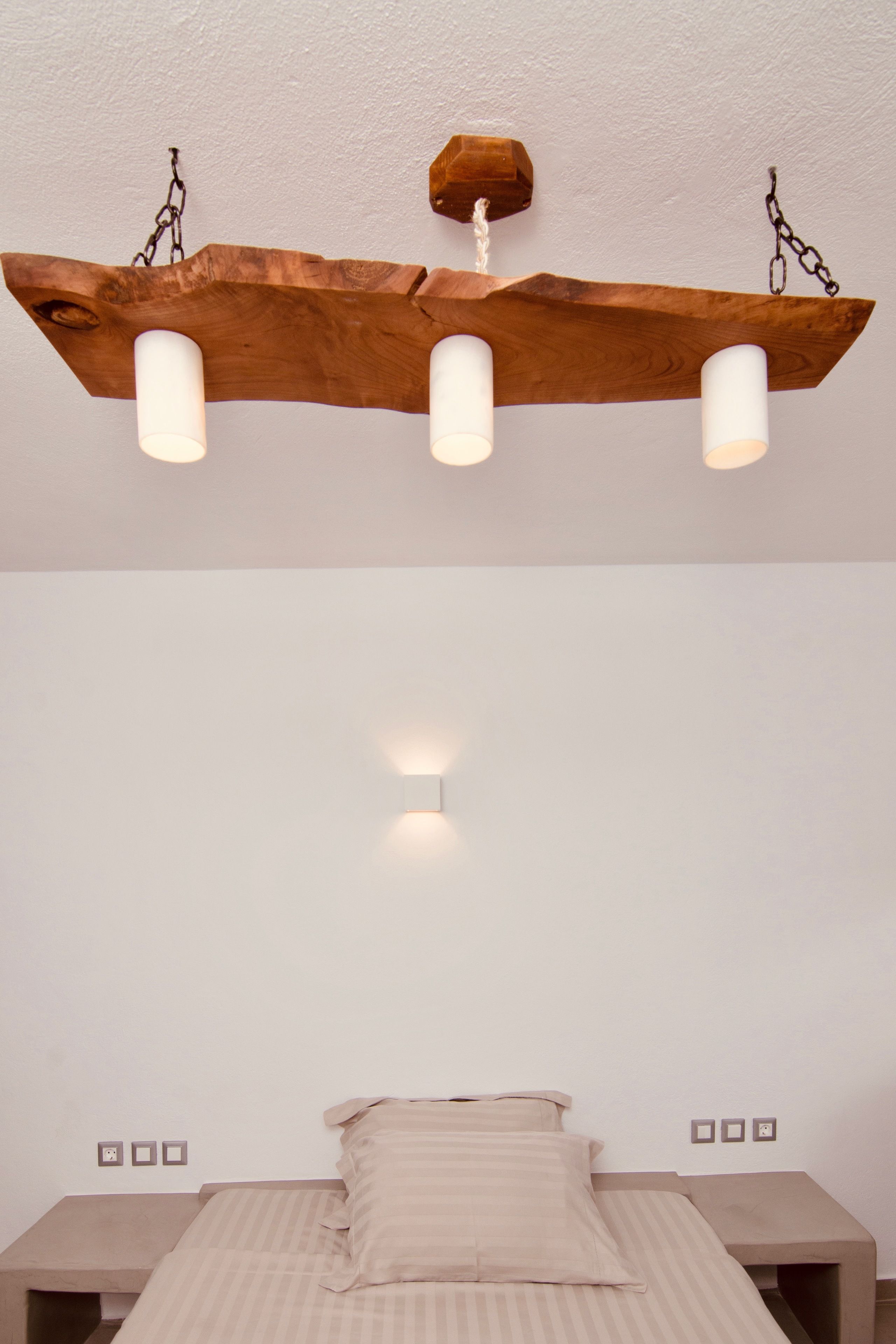 A bedroom with a wooden ceiling light fixture, a bed with a striped bedspread, and bedside tables.