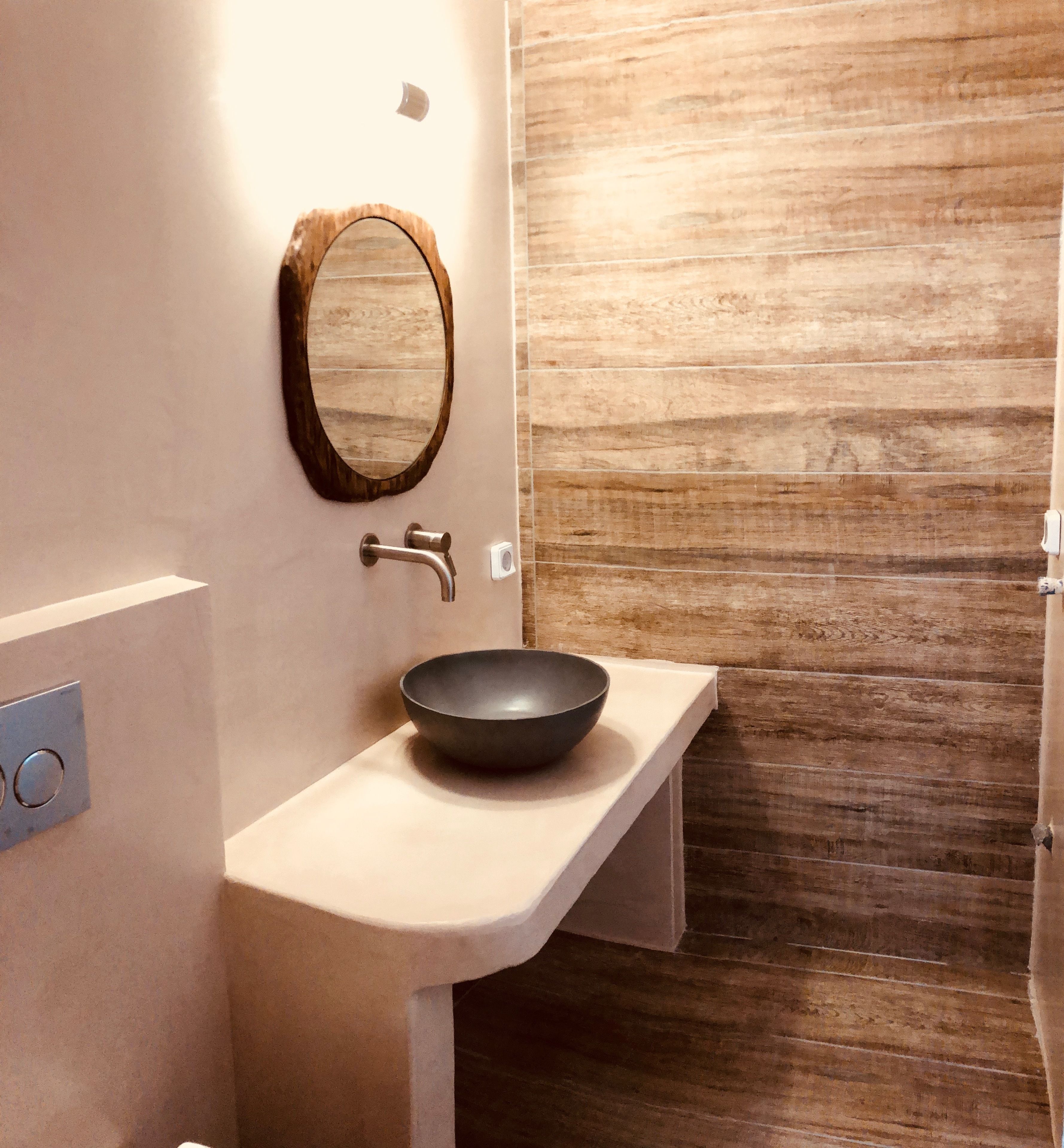 Un baño con un lavamanos color crema, un espejo con marco de madera y una pared de madera.