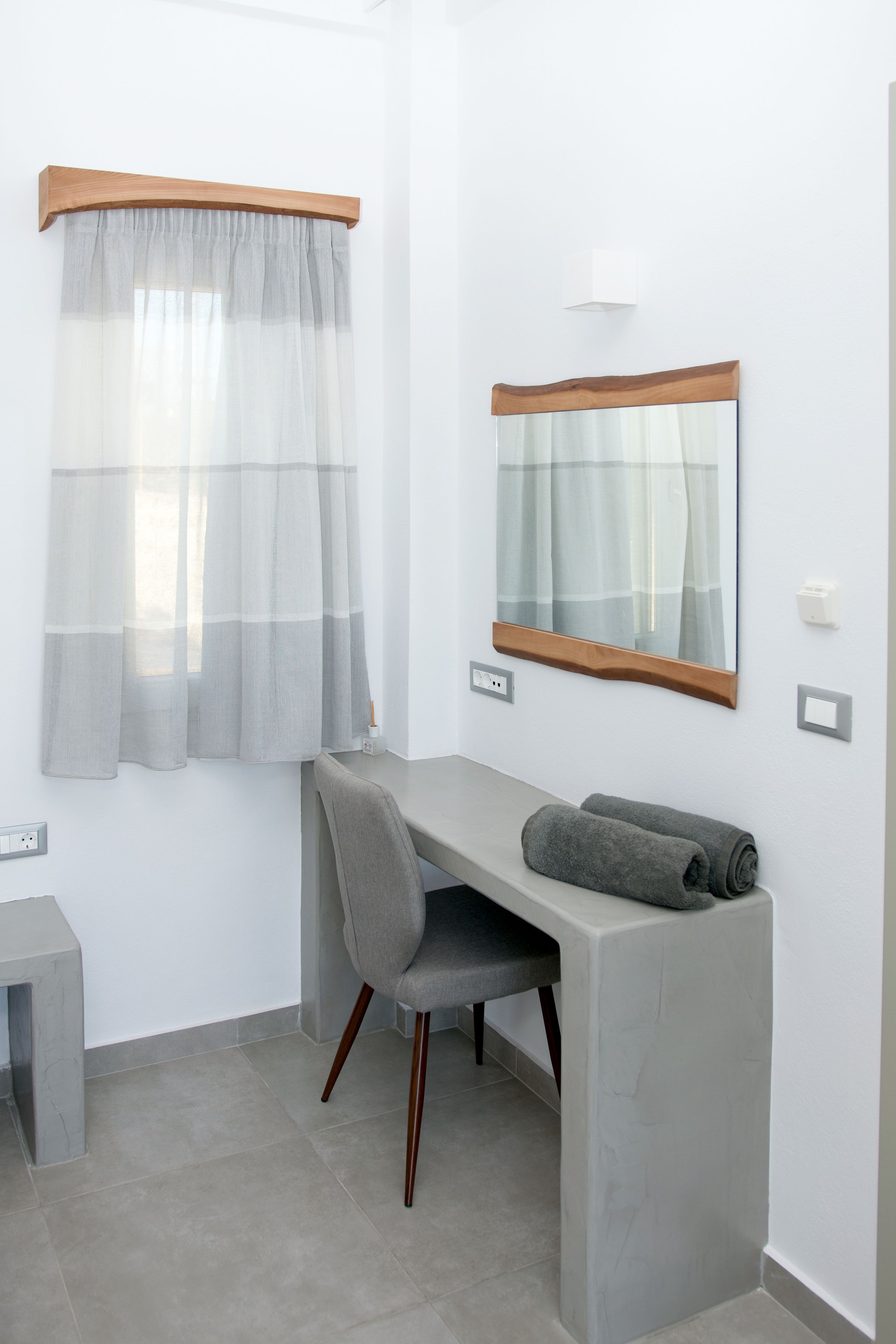 A modern bathroom with a grey vanity, a mirror, and a window with sheer curtains.