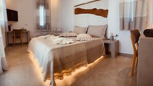 A bedroom with a large bed, bedside tables, a desk, and a chair. - Aeris suites (Naxos)