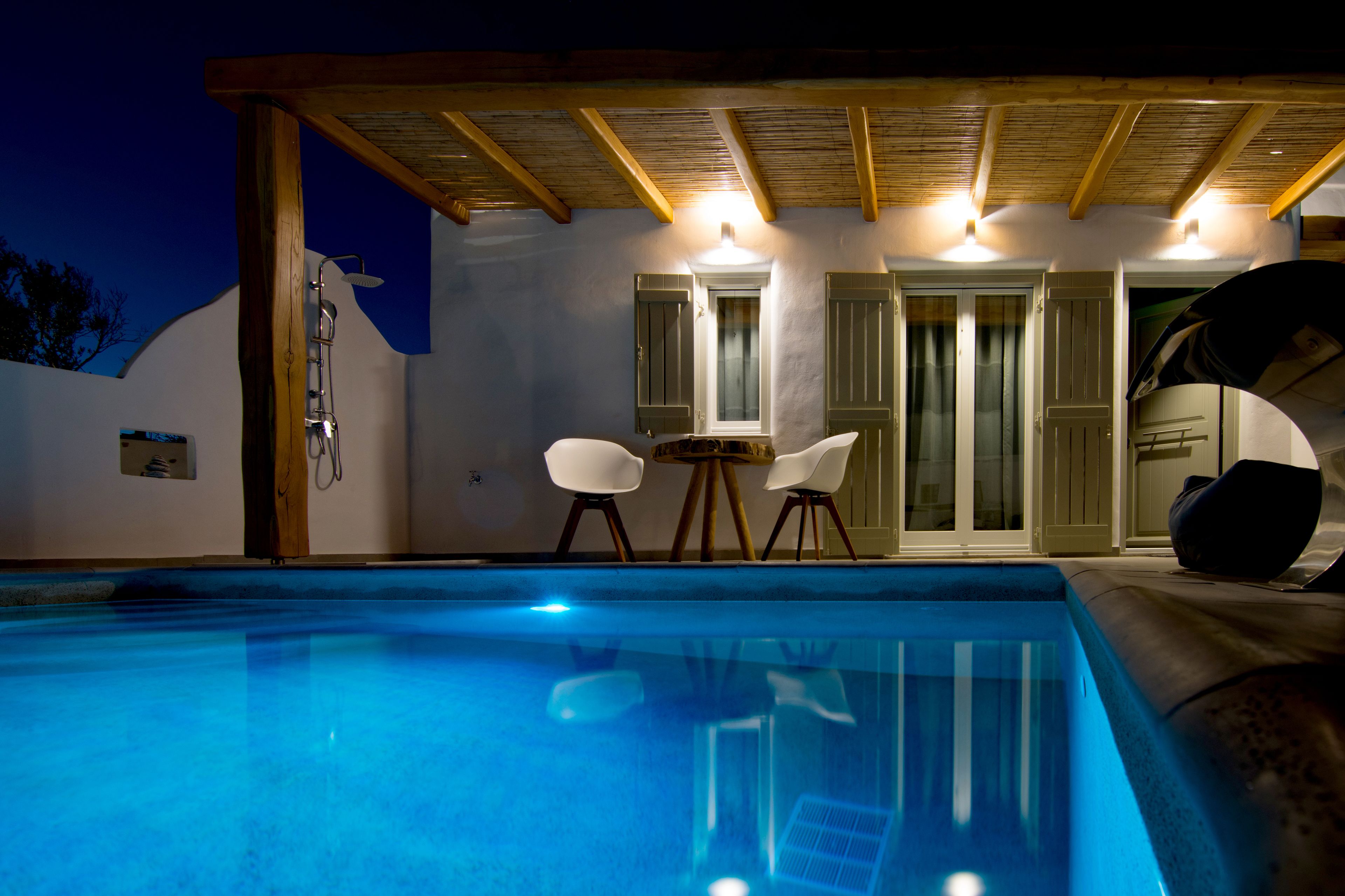 A swimming pool with a wooden pergola overhead, two white chairs, and a door with glass panels.