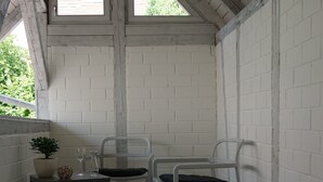 A small, enclosed balcony with a sloped ceiling, white brick walls, and two metal chairs.