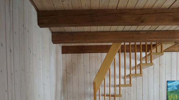 A wooden staircase in a room with a television, a woven basket, and a painting on the wall.