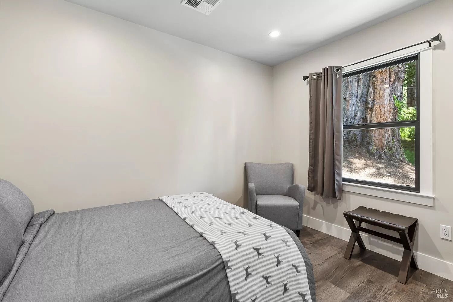 Una camera da letto con un letto, una sedia, un tavolino e una finestra vista alberi.