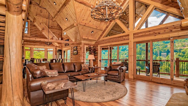 A spacious living room with a wooden ceiling, leather furniture, and large windows offering a view of the outdoors.