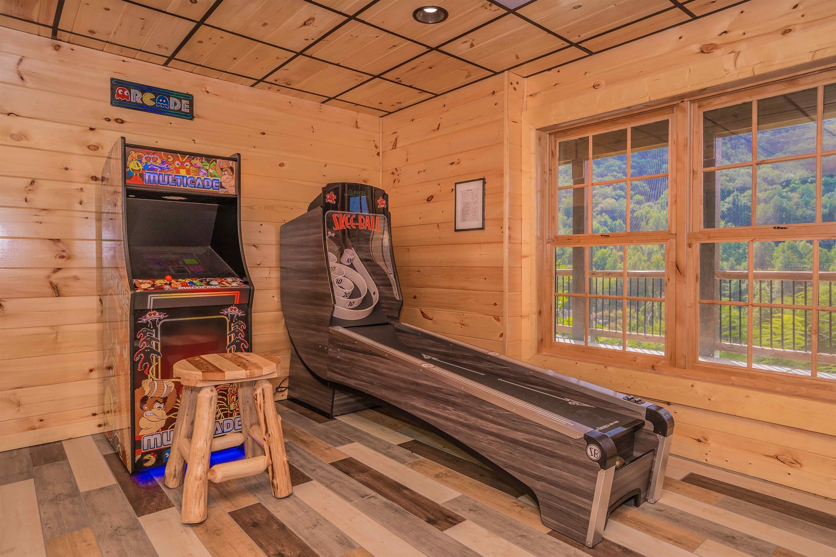 Una habitación de madera con juegos de arcade, una mesa de billar y un ventanal con vistas a árboles.