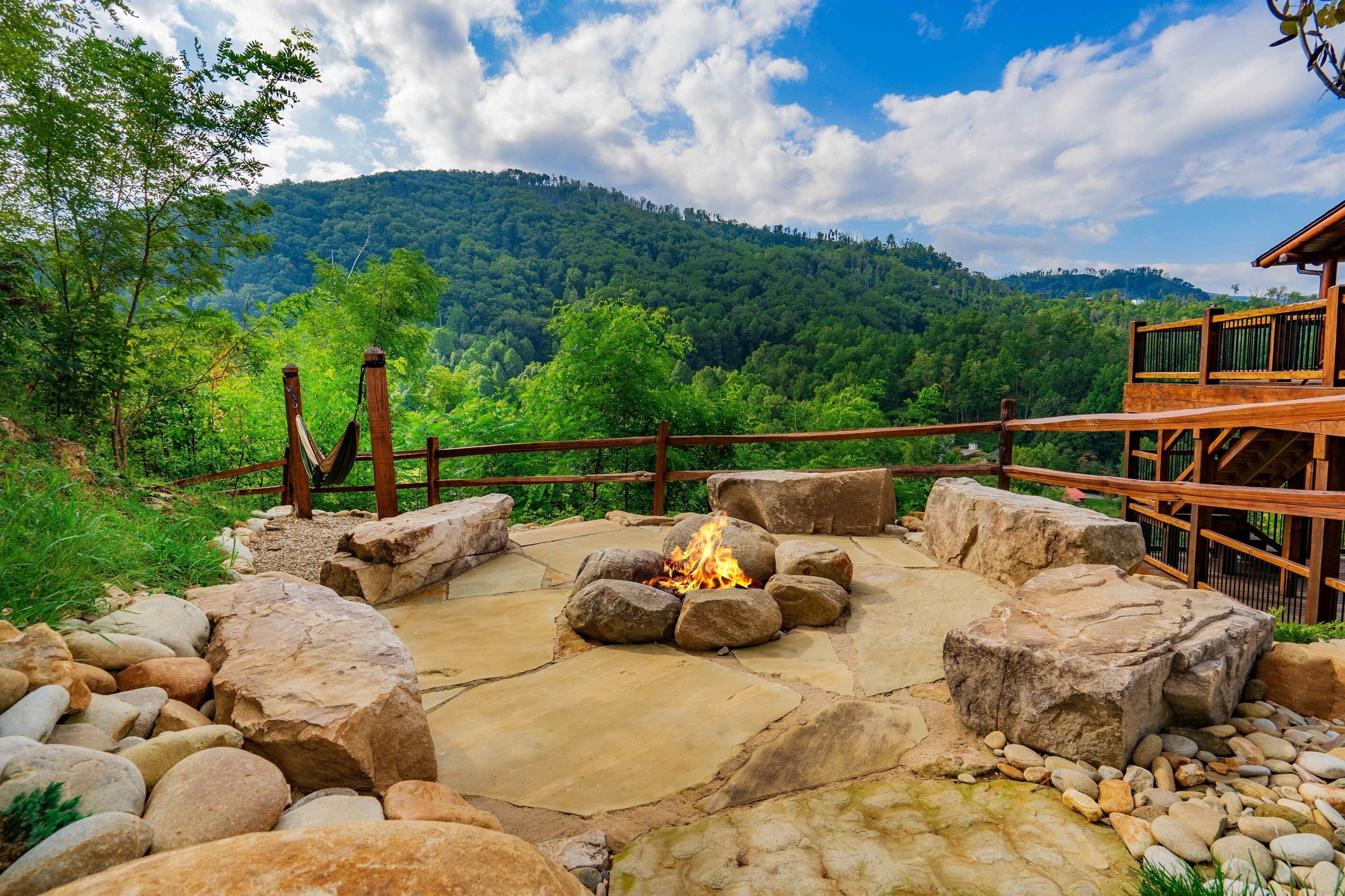 A stone fire pit surrounded by rocks, a wooden deck, and a mountainous backdrop.