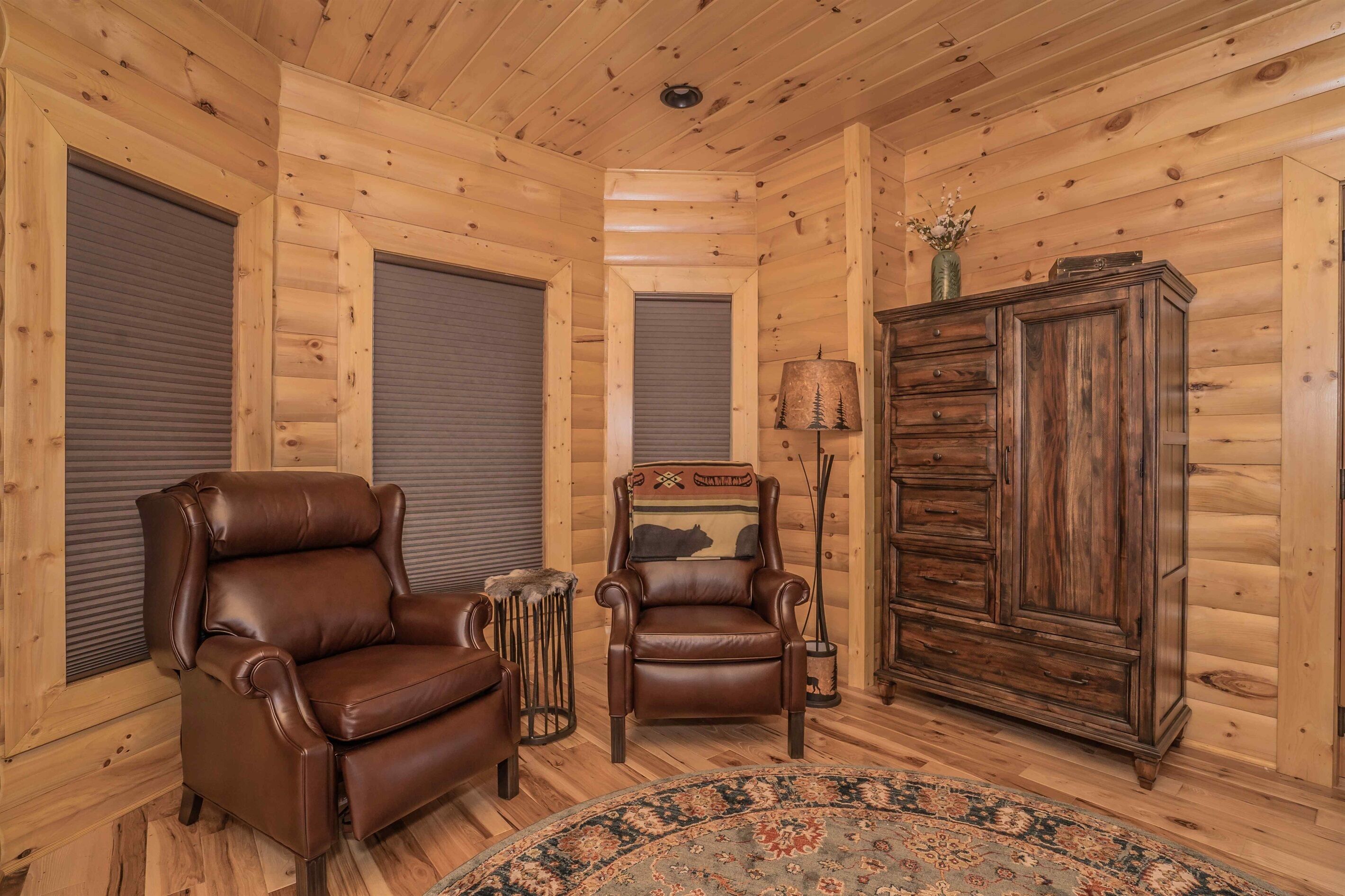 L’intérieur d’une cabane en rondins, avec deux fauteuils en cuir, un meuble en bois et un tapis à motifs.