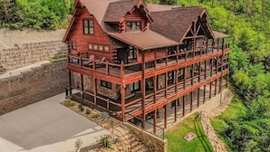 A multi-story log cabin with a stone foundation, multiple balconies, and a surrounding stone wall.