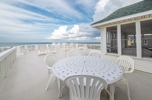 A covered outdoor area with a round table and white chairs, overlooking the ocean.