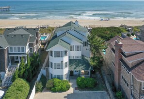 A multi-story residential building with a prominent balcony, a swimming pool, and a beach view.
