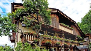 A traditional wooden chalet with balconies, surrounded by lush greenery.