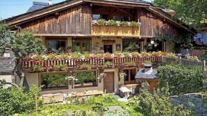 A traditional wooden chalet with a balcony adorned with flowers, a stone foundation, and a rustic exterior.